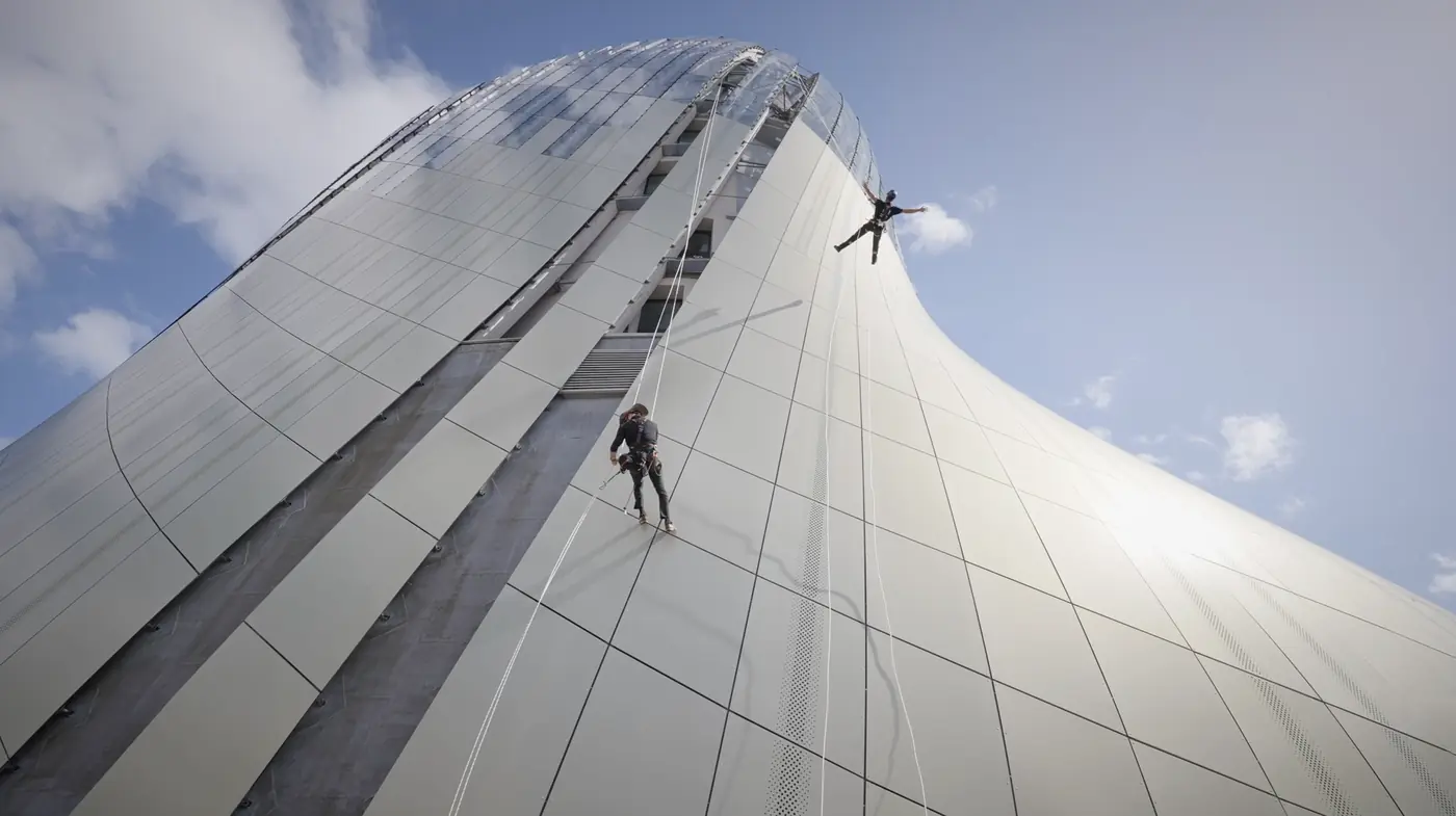 Deux cordistes en rappel sur la façade courbe de la Cité du Vin, sous un ciel bleu.