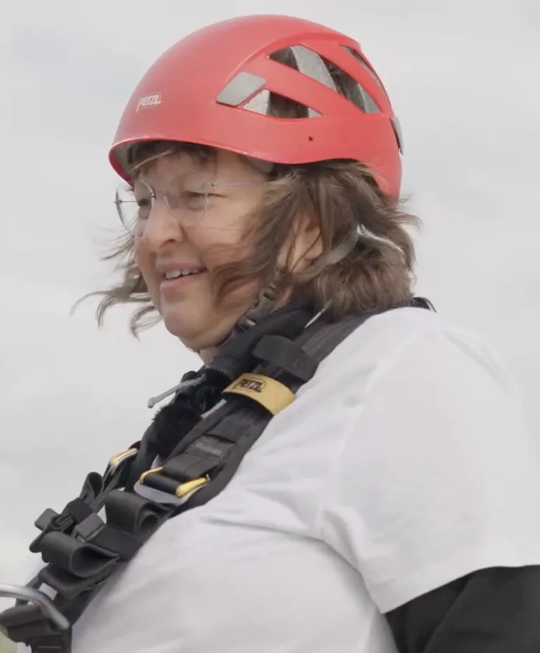 Portrait de Claire, Athlète du Vertige : casque rouge, cheveux au vent, souriante, de profil.