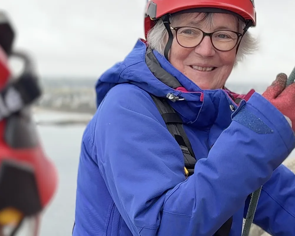 Portrait de Jacqueline, Athlète du Vertige : souriante, veste bleue et casque rouge, sur le phare de l'Île Vierge.