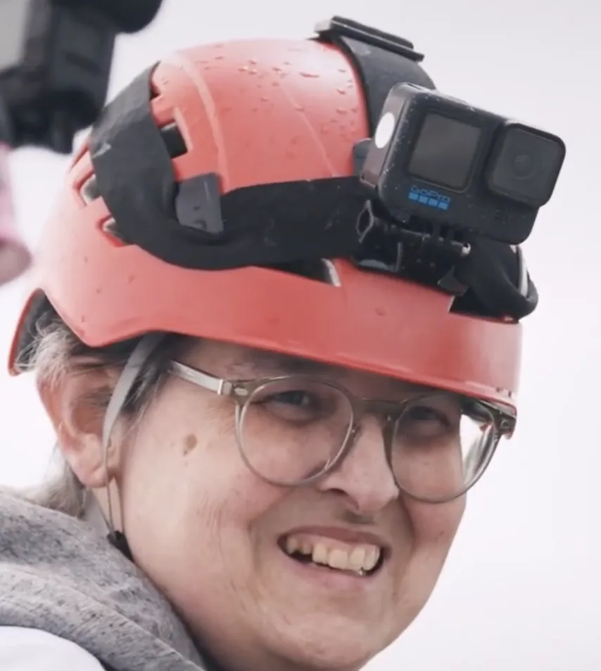 Portrait de Sonia, Athlète du Vertige : casque rouge équipé d'une caméra, lunettes, grand sourire.