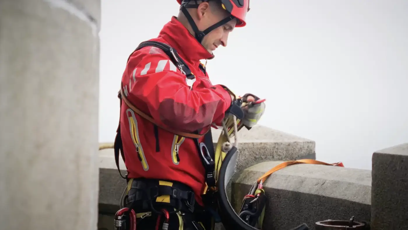 Un secouriste en tenue rouge prépare son équipement de rappel en haut du phare.